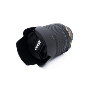 Nikon 18-105mm f35-56 G ED DX VR-3 Nikon-kameran objektiivi, johon on kiinnitetty vastavalosuoja ja objektiivin suojus, valkoisella taustalla.
