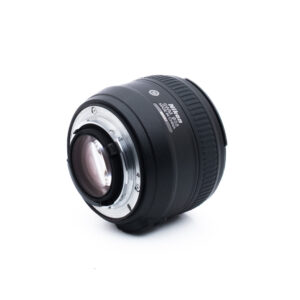 Nikon 50mm f14 G-1-2 Musta Nikon-kameran objektiivi, jossa on hopeinen metallinen kiinnitysrengas, vinossa valkoisella taustalla. Objektiivin merkinnät ja kiinnityskontaktit ovat näkyvissä.