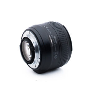 Musta Nikon-kameran objektiivi, jossa on hopeinen metallikiinnike, on sijoitettu valkoiselle taustalle, ja siinä näkyy takanäkymä ja sivulle on painettu joitakin tuotetietoja.
