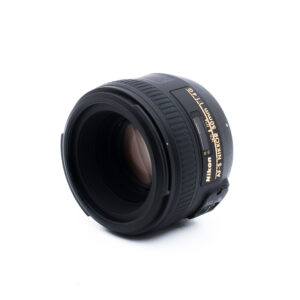Nikon 50mm f14 G-2-2 Musta Nikon AF-S NIKKOR 50mm f/1.8G -kameran objektiivi valkoisella pohjalla, jossa on kulma, jossa näkyy lasielementti ja kultaiset tuotemerkin yksityiskohdat.