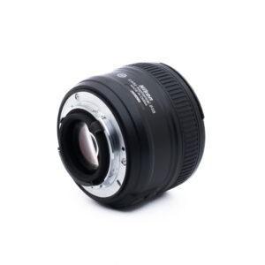 Nikon 50mm f18 G-1-5 Nikon AF-S NIKKOR 50mm f/1.8G -kameran objektiivi näkyy valkoisella pohjalla, ja sen kulma osoittaa metallisen objektiivin kiinnikkeen ja osan mustasta, uurretusta tarkennusrenkaasta.