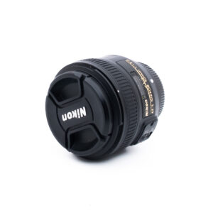 Nikon 50mm f18 G-3-5 Nikon-kameran objektiivi, johon on kiinnitetty objektiivin suojus ja jossa näkyy tuotemerkki ja objektiivin yksityiskohdat valkoisella taustalla.