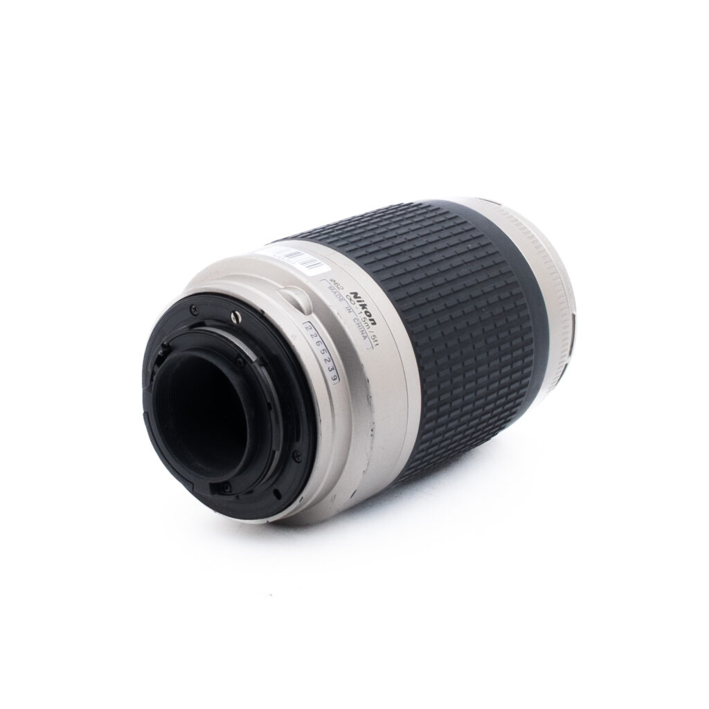 Nikon AF Nikkor 70-300mm f4-56 G-1 Nikon-kameran objektiivi, jossa on hopeanvärinen ja musta runko, kuvassa kyljellään siten, että kiinnityspää osoittaa eteenpäin, ja siinä näkyvät objektiivin koskettimet ja bajonettikiinnitys.