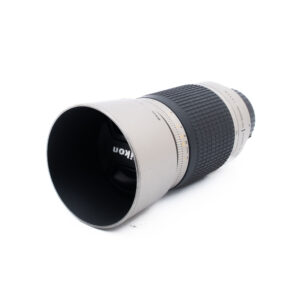 Nikon AF Nikkor 70-300mm f4-56 G-3 Hopeanvärinen ja musta Nikon-kameran objektiivi, jossa on kuvioitu kahva ja pidennetty linssinsuojus ja joka on sijoitettu vinoon valkoiselle taustalle.