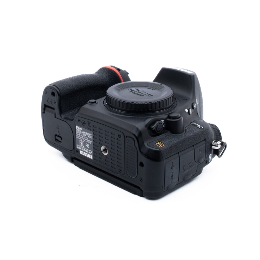 Nikon D750 5512-1 Mustan Nikon DSLR-kameran runko on kuvassa kyljellään, jossa näkyy pohja ja osa kahvasta, objektiivin kiinnityssuojus on paikallaan ja useita liitäntäportteja ja merkintöjä on näkyvissä.