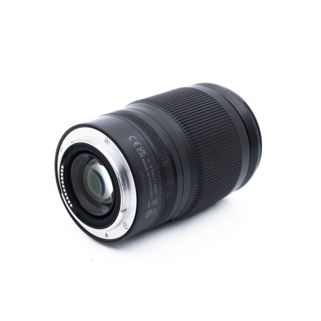 Nikon Z 24-200mm f4-63 VR-1-3 Musta kameran objektiivi, jossa on kuvioitu kahva, on sijoitettu valkoiselle taustalle, ja siinä näkyy metallinen kiinnitys ja elektroniset koskettimet katsojaa kohti.