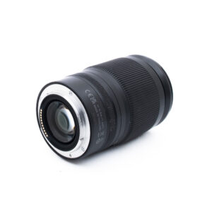 Nikon Z 24-200mm f4-63 VR-1-3 Musta kameran objektiivi, jossa on kuvioitu kahva, on sijoitettu valkoiselle taustalle, ja siinä näkyy metallinen kiinnitys ja elektroniset koskettimet katsojaa kohti.