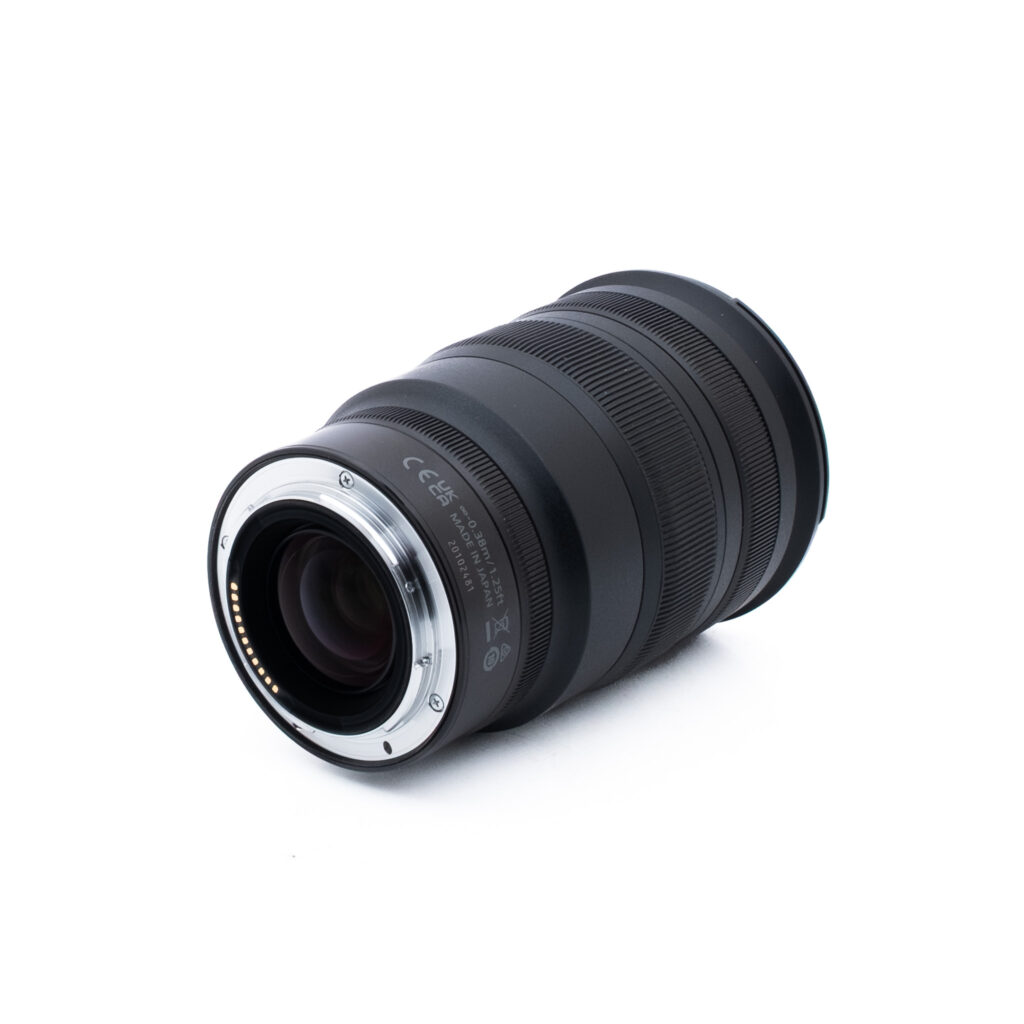 Nikon Z 24-70mm f28 S-1-2 Musta kameran zoom-objektiivi, jossa on kuvioitu kahva, metallinen kiinnitysrengas ja elektroniset koskettimet, sijoitettu vinoon valkoiselle taustalle.