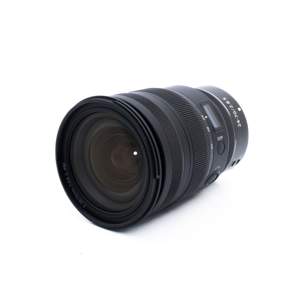 Nikon Z 24-70mm f28 S-2-2 Musta kameran zoom-objektiivi, jossa on uurteiset tarkennus- ja zoomausrenkaat ja jossa on merkintä "24-70mm 1:2.8 S", on kuvattu kulmassa valkoisella pohjalla.