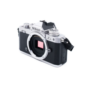 Nikon Z fc-4 Nikon Z fc (SC 6500) - Käytetty hopeanvärinen ja musta peilitön kamerarunko ilman objektiivia, jossa on kenno ja retro-muotoilu valkoista taustaa vasten.