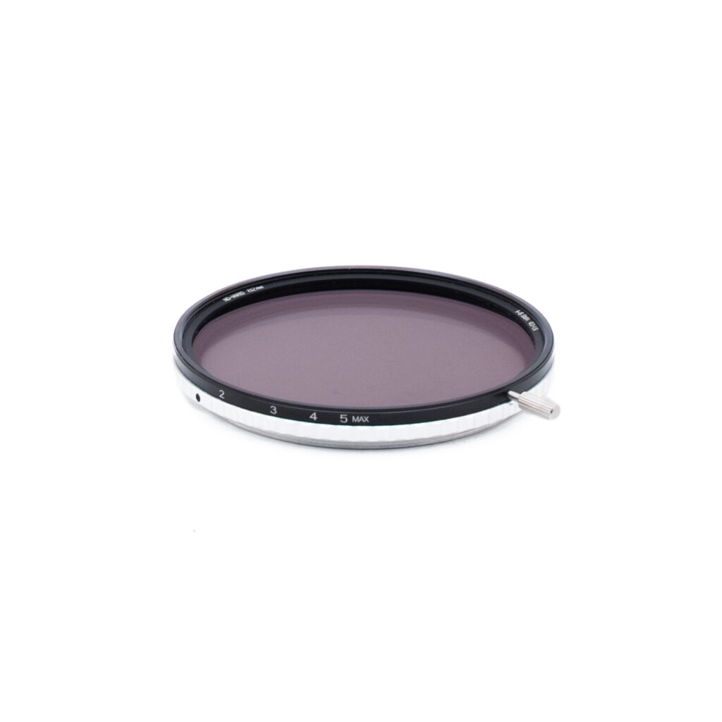 Nisi ND-Vario 82mm-1 Ympyränmuotoinen kameran linssisuodatin, jossa on musta ja hopeinen reunus, numeroitu 1-5 ja merkitty MAX. Suodattimen sivussa on pieni metallivipu, ja se on asetettu valkoista taustaa vasten.