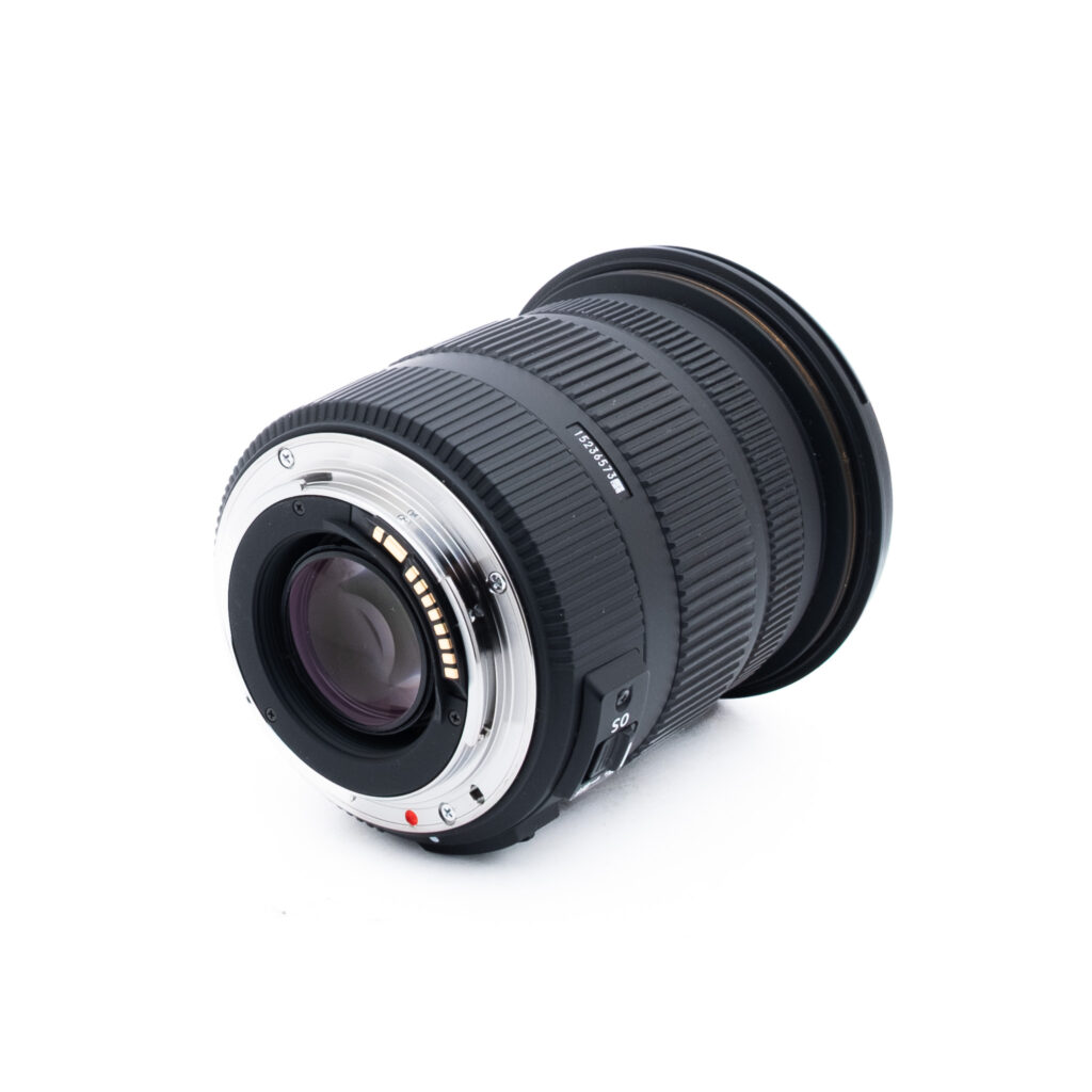 Sigma 17-50mm f28 EX DC OS HSM Canon-1-2 Musta kameran objektiivi, jossa on kuvioitu kahva ja metallinen kiinnitysrengas, on sijoitettu valkoiselle taustalle, ja siinä näkyvät takaelementti ja elektroniset koskettimet.