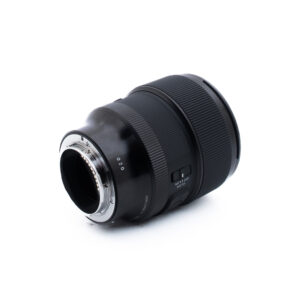 Sigma 85mm f14 DG DN Sony-1-5 Musta kameran objektiivi, jonka kiinnityspäässä on elektroniset koskettimet näkyvissä, valkoisella pohjalla, ja sivussa on tarkennus- ja kytkinohjaimet.