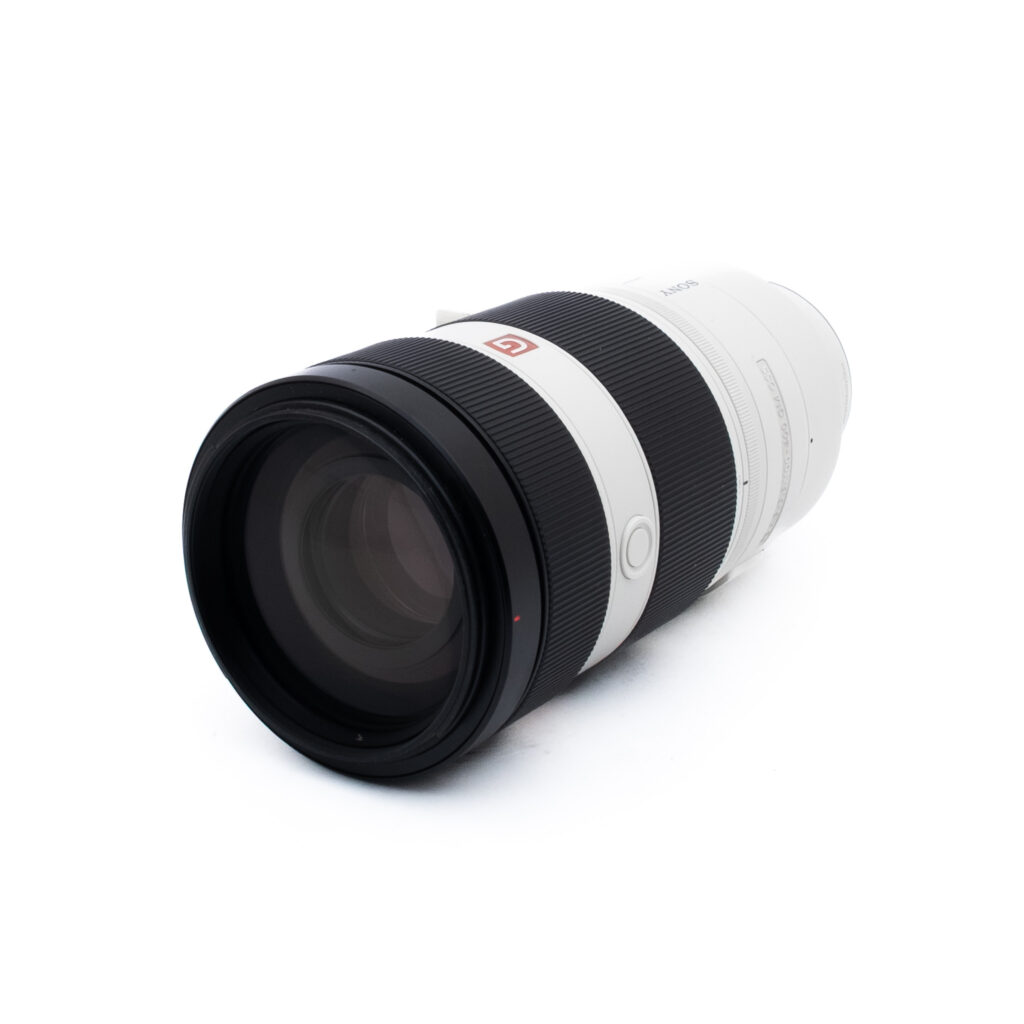 Sony 100-400 GM-2 Ammattilaiskameran telezoom-objektiivi, jossa on musta etupuoli ja valkoinen tynnyri, makaa kyljellään valkoista taustaa vasten.