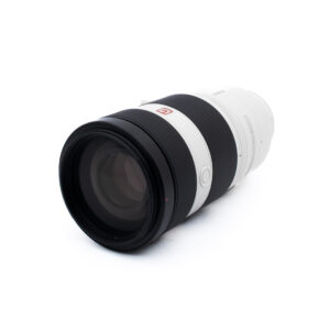Sony 100-400 GM-2 Ammattilaiskameran telezoom-objektiivi, jossa on musta etupuoli ja valkoinen tynnyri, makaa kyljellään valkoista taustaa vasten.