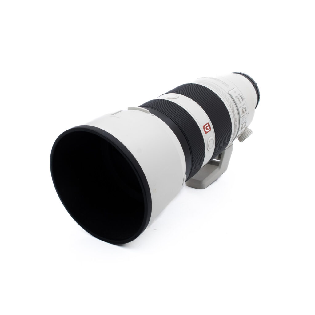 Sony 100-400 GM-3 Suuri valkoinen teleobjektiivi, jossa on musta kuminen kahva, punainen G-logo ja jalustakiinnike, sijoitettu vinoon valkoiselle taustalle.