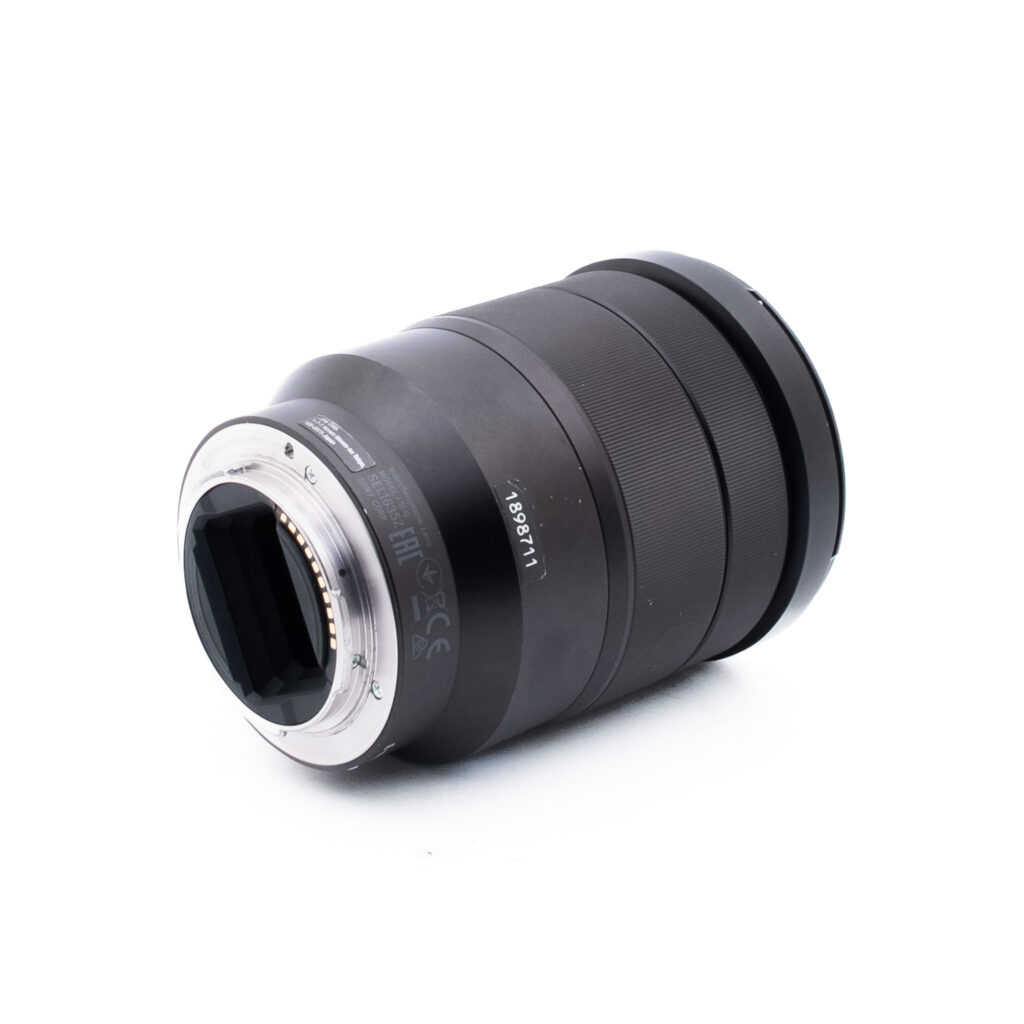 Sony 16-35mm f4 ZA OSS-1-3 Musta kameran linssi kyljellään, josta näkyy metallikiinnitys ja elektroniset kontaktit. Tynnyrissä on kuvioidut pitorenkaat ja painetut mallinumerot, eikä objektiivin lasi ole näkyvissä. Taustalla on pelkkä valkoinen.