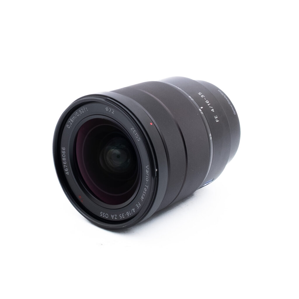 Sony 16-35mm f4 ZA OSS-2-3 Musta kameran linssi, jossa on näkyviä lasielementtejä ja merkintöjä ja joka lepää vinossa valkoisella pohjalla.