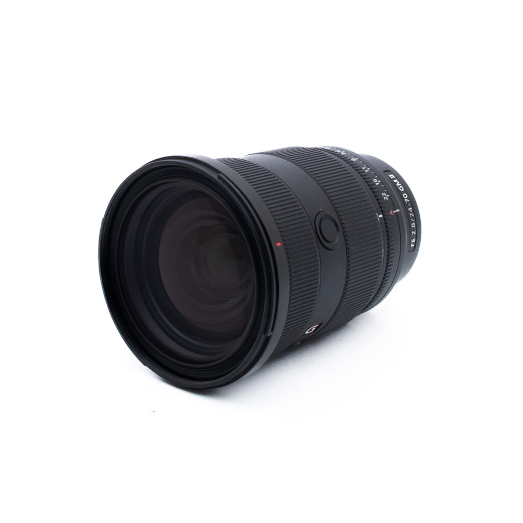 Sony 24-70mm f28 GM II-2 Musta kameran objektiivi, jossa on kuvioidut zoomaus- ja tarkennusrenkaat, näkyy valkoisella pohjalla hieman vinossa, jolloin etulasi ja osa piipusta tulevat esiin.