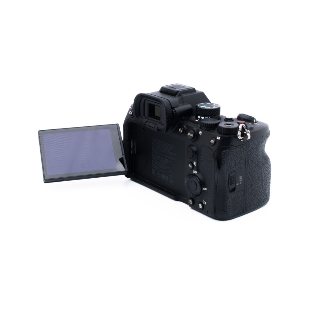 Sony A7 IV 3766-3 Musta digitaalikamera, jossa on vasemmalle ulosvedettävä LCD-näyttö, kuvattuna takaa hieman oikealle valkoisella pohjalla.