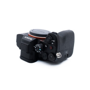 Sony A7R V 0622-2 Musta Sony-digitaalikameran runko näkyy kuvassa ylhäältä päin kuvattuna, ja siinä on valintakiekkoja, painikkeita ja kuvioitu kahva; objektiivi ei ole kiinnitettynä, joten objektiivin kiinnityssuojus on näkyvissä.