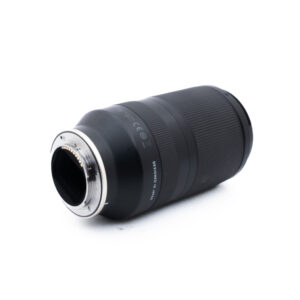 Tamron 70-180mm f28 Di III VXD-1 Musta kameran linssi makaa kyljellään, vasemmassa päässä näkyvät metallinen kiinnitysrengas ja elektroniset koskettimet valkoista taustaa vasten.