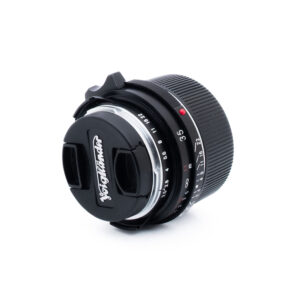 Voigtländer 35mm f25-3 Valkoisella pohjalla on Voigtländer-kameran objektiivi, jossa on musta objektiivin suojus ja jossa on merkitty aukko- ja tarkennusasetukset.