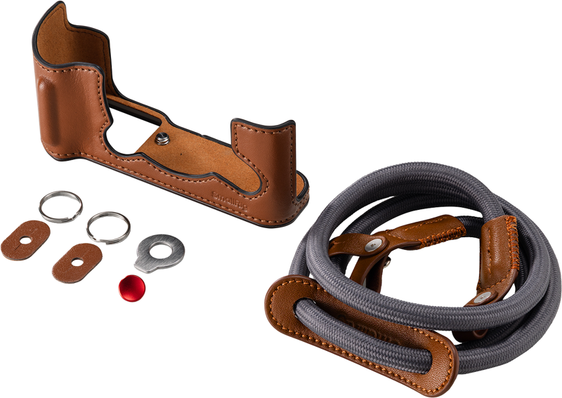 800q-01_135078 SmallRig 5670 Leather Half Case Kit for Fujifilm X-T30/II/III (ruskea) sisältää ruskean nahkaisen puolikotelon, yhteensopivan hihnan nahkakoristeilla, kaksi metallirengasta, kaksi nahkaista rengassuojaa, metallisen aluslevyn ja pienen punaisen painikkeen vaalealla pohjalla.