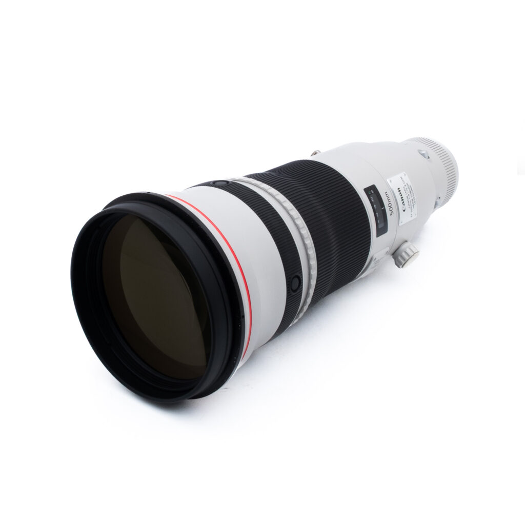 Canon 500mm f28 L II IS USM-2 Canon EF 500mm f/4 L IS II USM (Kunto K5, Takuu 6kk) - Käytetty on suuri ammattikäyttöön tarkoitettu teleobjektiivi, jossa on valkoinen runko, musta kahva ja kiinnitysteline ja joka on kuvattuna vinossa valkoista taustaa vasten.