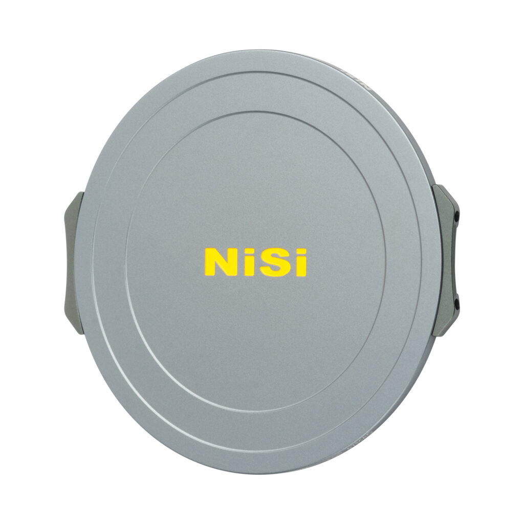 NisiMag67_13 NiSi JetMag Pro 67mm Magnetic Front Cap -etutulppa on pyöreä, hopeinen linssinsuojus, jonka keskellä on rohkea keltainen NiSi-tuotemerkki, sen sileässä pinnassa on hienovaraiset pyöreät urat ja sivuilla metalliklipsit.