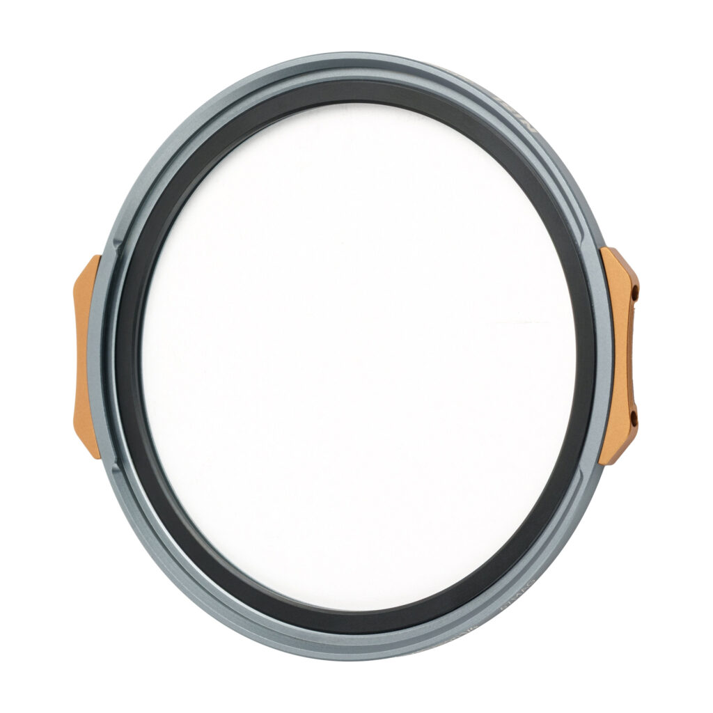 NisiMag67_6 Pyöreä, litteä NiSi JetMag Pro 67mm Black Mist 1/4 -suodatin, jossa on harmaa ja kultainen reunus ja valkoinen keskus, joka muistuttaa kameran linssinsuojusta, näkyy valkoista taustaa vasten.