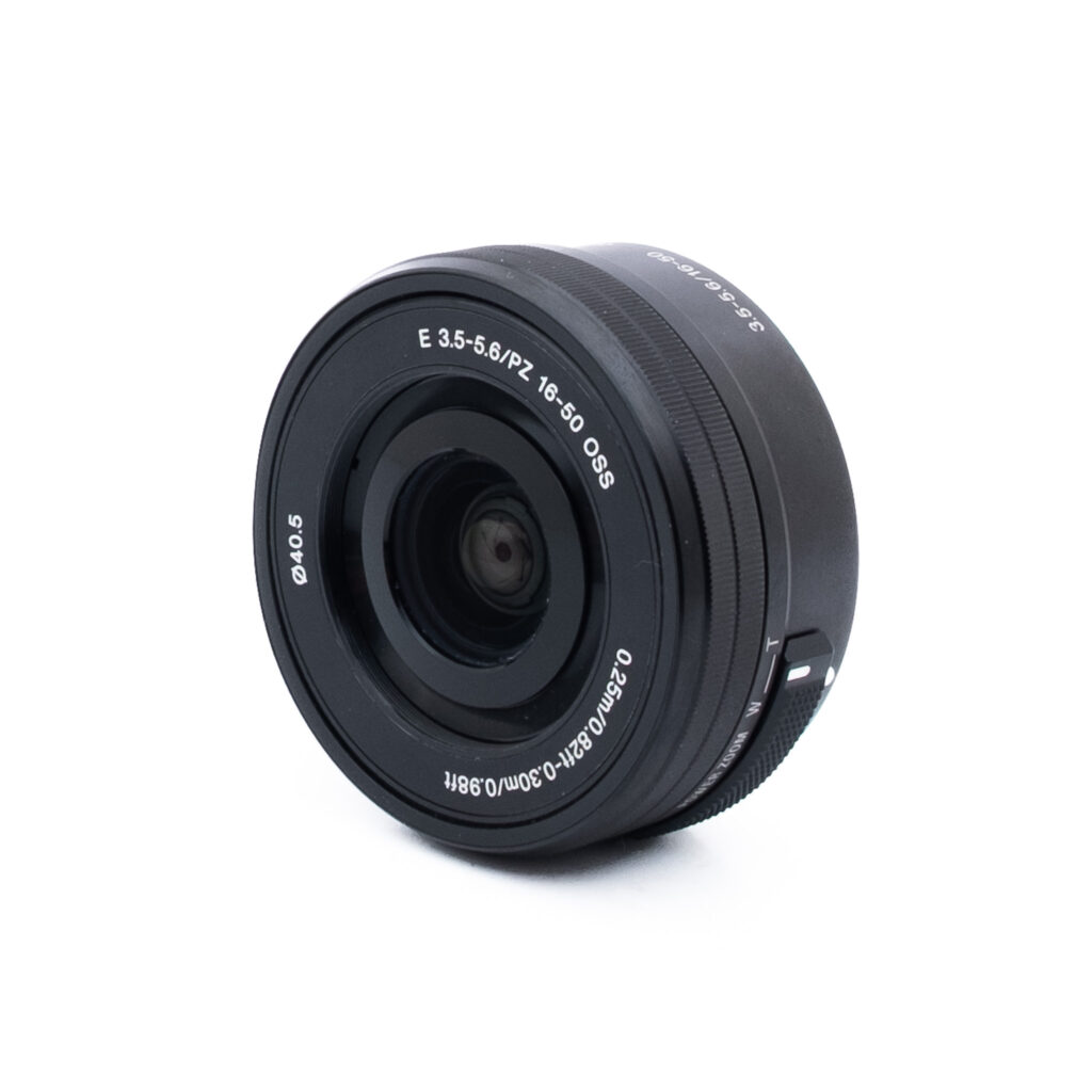 Sony 16-50 pz Sony E 16-50mm f/3.5-5.6 PZ OSS - Käytetty -objektiivi, jossa on valkoiset tiedot, kuten "E 3.5-5.6/PZ 16-50 OSS" ja "Ø40.5", kuvattuna kulmassa valkoista taustaa vasten.